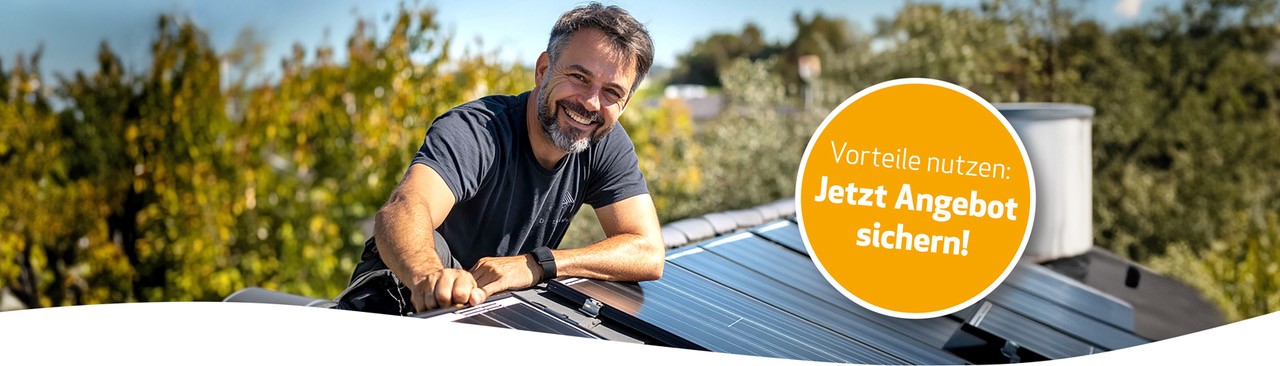 Lächelnder Monteur installiert Solarmodule auf einem Hausdach bei Sonnenschein
