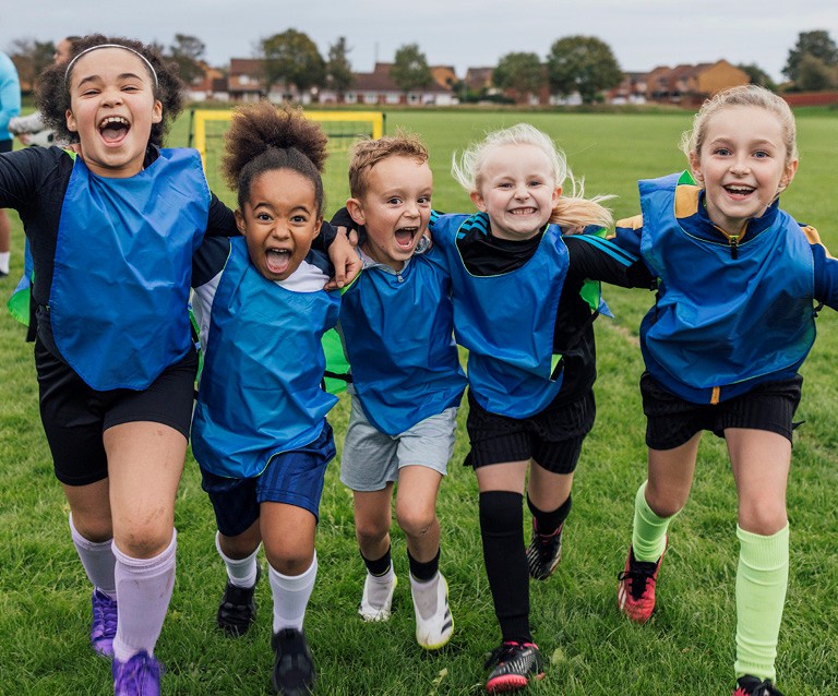 Fünf Kinder rennen lachend über ein Spielfeld und zeigen Teamgeist bei einem Sportprojekt in Meerbusch.