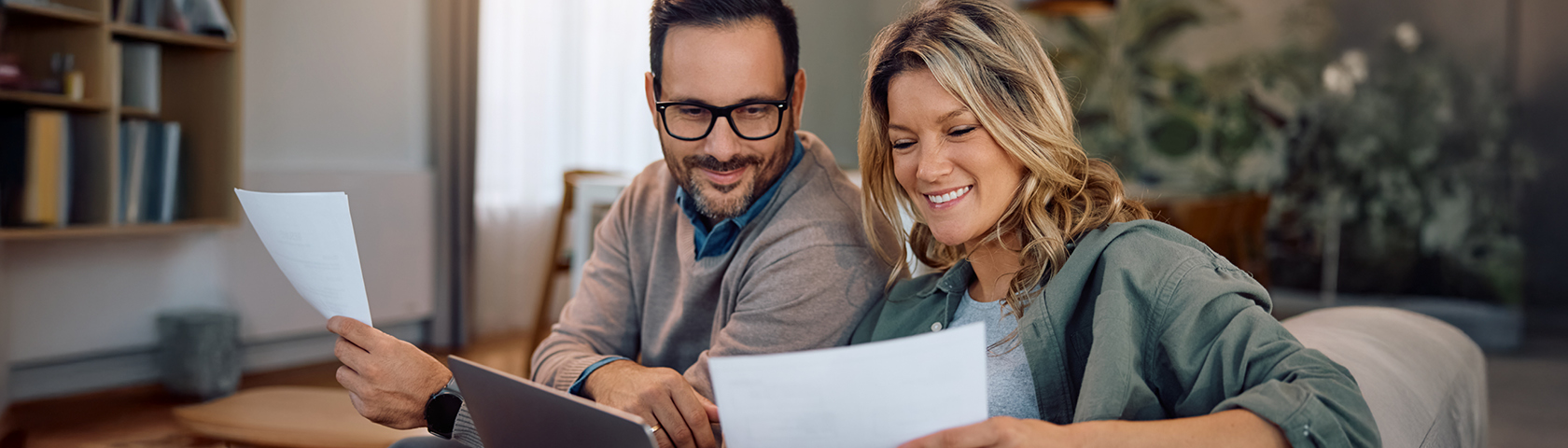 Ein Paar sitzt auf dem Sofa, lächelt und prüft gemeinsam Stromrechnungen – Symbolbild für transparente Energiepreise und Kundennähe