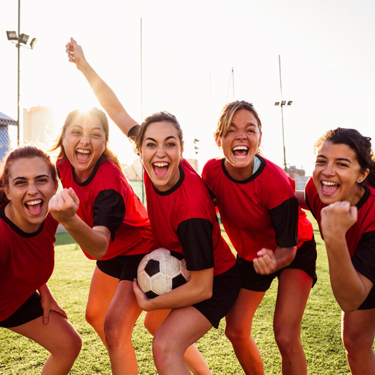 Frauenfußballteam in roten Trikots posiert mit Ball auf dem Spielfeld